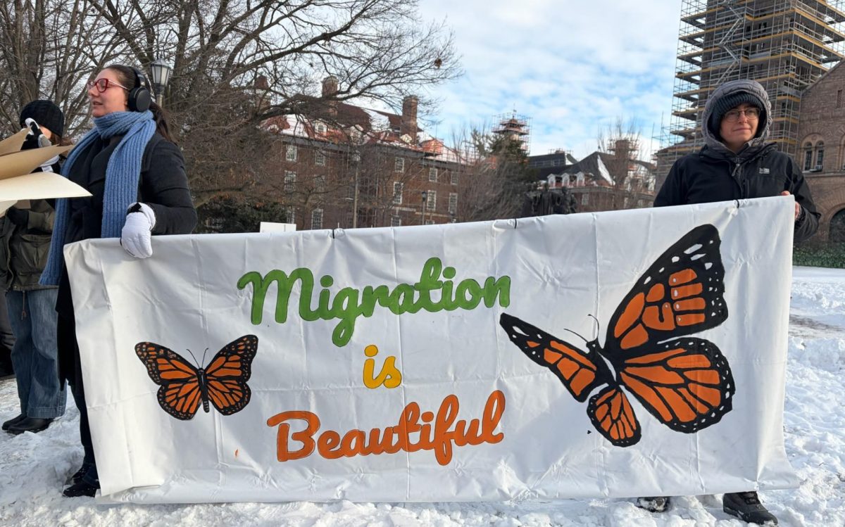 Community members hold up a banner reading "Migration is Beautiful" at the Alma Mater.